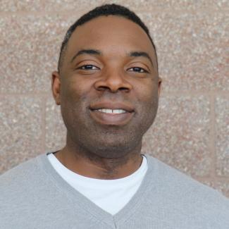 Headshot of Frank, a male-presenting person with dark skin tone, short dark hair, wearing a light grey sweater.