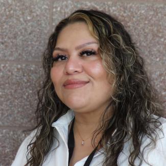 Headshot of Gina, a female-presenting person with medium skin tone, long, dark, curly hair, wearing a white blouse.