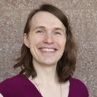 Headshot of Josie, a female-presenting person with light skin tone, shoulder-length brown hair, wearing a dark red shirt.